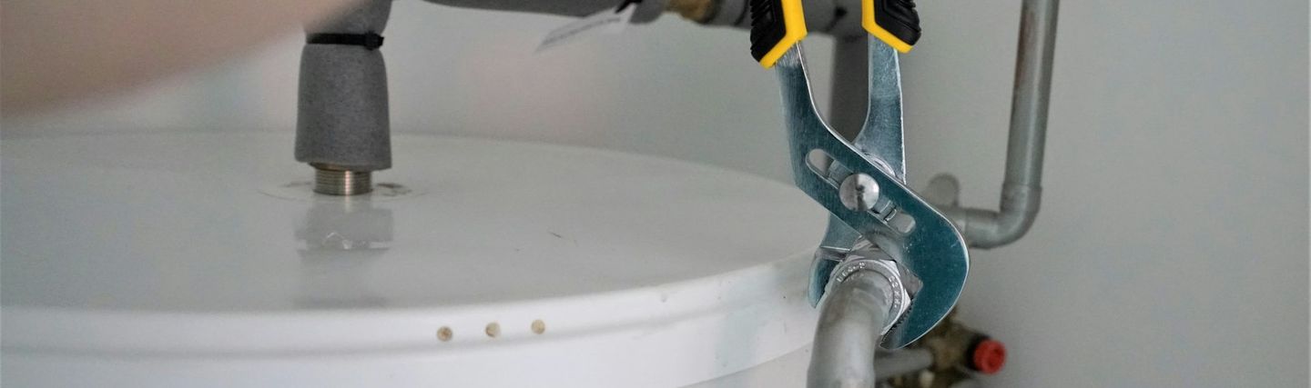 Technician tightening a water heater fitting with a pair of pliers